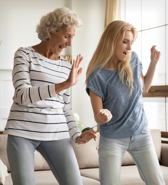 An elder woman and a young woman dancing in a livingroom.